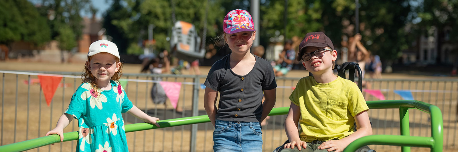 Three children stand on an inclusive roundabout, looking at the camera and smiling.